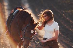 giovane donna nel protettivo cappello a piedi con sua cavallo nel agricoltura campo a soleggiato giorno foto