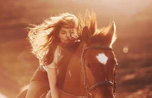 giovane donna nel protettivo cappello con sua cavallo nel agricoltura campo a soleggiato giorno foto