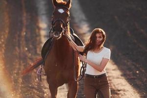 giovane donna nel protettivo cappello a piedi con sua cavallo nel agricoltura campo a soleggiato giorno foto