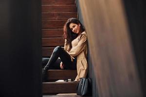 allegro brunetta nel nero ghette seduta su di legno le scale e sorridente foto