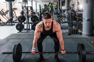 sollevamento bilanciere. giovane allegro forte uomo nel nero indossare avere allenarsi giorno nel Palestra foto