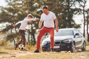 giocando calcio. padre con il suo figlio la spesa fine settimana insieme all'aperto vicino foresta a giorno foto