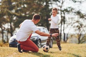 giocando calcio. padre con il suo figlio la spesa fine settimana insieme all'aperto vicino foresta a giorno foto