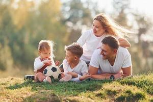 con calcio sfera. contento famiglia dire bugie giù all'aperto vicino il foresta. con figlia e figlio foto