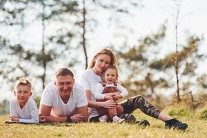 seduta e dire bugie su il terra. contento famiglia la spesa fine settimana insieme all'aperto vicino il foresta. con figlia e figlio foto