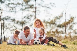 seduta e dire bugie su il terra. contento famiglia la spesa fine settimana insieme all'aperto vicino il foresta. con figlia e figlio foto