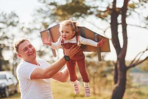 padre con il suo poco figlia avere divertimento all'aperto con fatto a mano di legno Ali foto