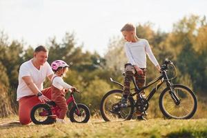 padre con il suo poco figlia e figlio avere divertimento con Bici all'aperto vicino il foresta foto