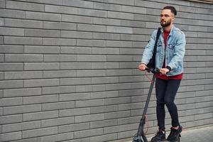 bello giovane tipo nel casuale Abiti equitazione elettrico schooter all'aperto a soleggiato giorno foto