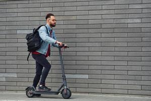 bello giovane tipo nel casuale Abiti equitazione elettrico schooter all'aperto a soleggiato giorno foto