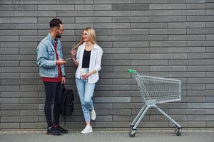 con shopping carrello. giovane elegante uomo con donna nel casuale Abiti all'aperto insieme. concezione di amicizia o relazioni foto