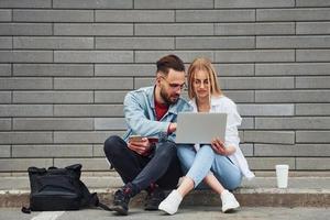 utilizzando il computer portatile. giovane elegante uomo con donna nel casuale Abiti seduta all'aperto insieme. concezione di amicizia o relazioni foto