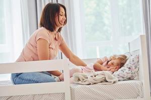 dormire volta. giovane madre con sua poco figlia nel casuale Abiti insieme in casa a casa foto