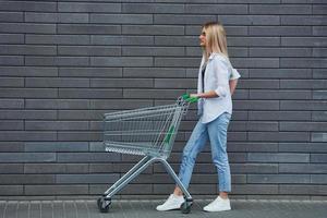 bellissimo bionda nel casuale Abiti con shopping carrello è all'aperto a soleggiato giorno foto