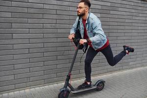 lato Visualizza di bello giovane tipo nel casuale Abiti quello equitazione elettrico schooter all'aperto a soleggiato giorno foto