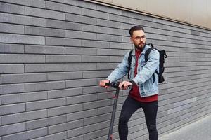 bello giovane tipo nel casuale Abiti equitazione elettrico schooter all'aperto a soleggiato giorno foto