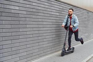 bello giovane tipo nel casuale Abiti equitazione elettrico schooter all'aperto a soleggiato giorno foto