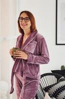 incinta giovane donna nel pigiama e bicchieri in piedi in casa a giorno foto