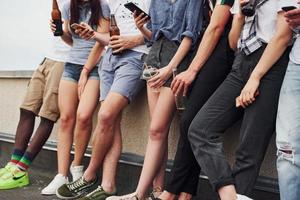 in piedi con telefoni e alcool nel mani. gruppo di giovane persone nel casuale Abiti avere un' festa a tetto insieme a giorno foto