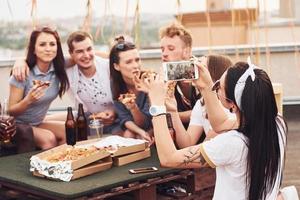 fabbricazione foto. delizioso Pizza. gruppo di giovane persone nel casuale Abiti avere un' festa a tetto insieme a giorno foto