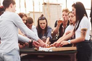 delizioso Pizza. gruppo di giovane persone nel casuale Abiti avere un' festa a tetto insieme a giorno foto