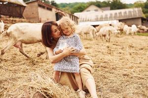 giovane madre con sua figlia è su il azienda agricola a estate con capre foto