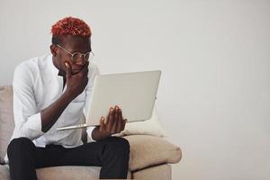 giovane africano americano uomo nel formale Abiti in casa con il computer portatile nel mani foto