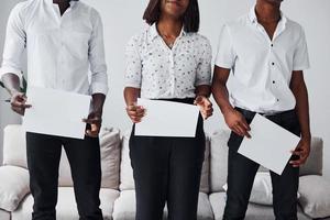 gruppo di africano americano persone nel formale Abiti in piedi vicino divano in casa nel ufficio insieme e Tenere vuoto documenti nel mani foto