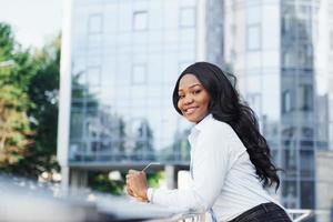 giovane afro americano donna nel bianca camicia all'aperto nel il città contro attività commerciale edificio foto