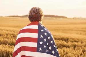 Visualizza a partire dal dietro a di patriottico anziano uomo quello in piedi su il campo con Stati Uniti d'America bandiera. concezione di la libertà foto