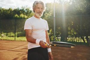 formazione volta. anziano moderno elegante uomo con racchetta all'aperto su tennis Tribunale a giorno foto