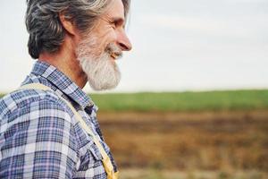 lato Visualizza. nel giallo uniforme. anziano elegante uomo con grigio capelli e barba su il agricolo campo con raccogliere foto