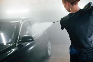 utilizzando attrezzatura con alto pressione acqua. moderno nero automobile ottenere puliti di donna dentro di auto lavare stazione foto