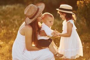 contento famiglia di madre, poco figlio e figlia la spesa gratuito tempo su il campo a soleggiato giorno tempo di estate foto