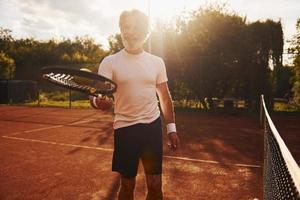 formazione volta. anziano moderno elegante uomo con racchetta all'aperto su tennis Tribunale a giorno foto