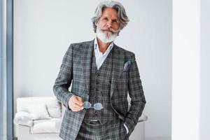 nel appartamento con elegante Abiti. anziano elegante moderno uomo con grigio capelli e barba in casa foto