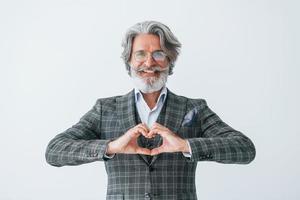 nel elegante Abiti. in piedi contro bianca parete. anziano elegante moderno uomo con grigio capelli e barba in casa foto