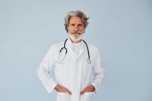 medico nel bianca cappotto contro parete. anziano elegante moderno uomo con grigio capelli e barba in casa foto