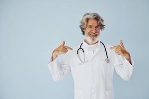 professionale positivo medico. anziano elegante moderno uomo con grigio capelli e barba in casa foto