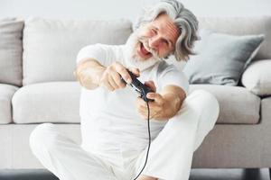giochi video gioco di utilizzando controllore. anziano elegante moderno uomo con grigio capelli e barba in casa foto