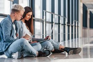 giovane maschio e femmina studenti seduta insieme su il pavimento con il computer portatile foto