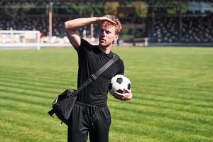 calcio giocatore su il campo. allegro giovane tipo nel nero camicia e pantaloni all'aperto a giorno foto