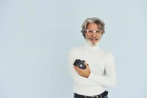 fotografo con Vintage ▾ telecamera. anziano elegante moderno uomo con grigio capelli e barba in casa foto