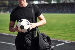 calcio giocatore su il campo. allegro giovane tipo nel nero camicia e pantaloni all'aperto a giorno foto