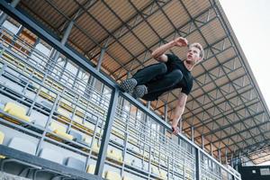 salto e fare parkour su il gradinate. allegro giovane tipo nel nero camicia e pantaloni all'aperto a giorno foto