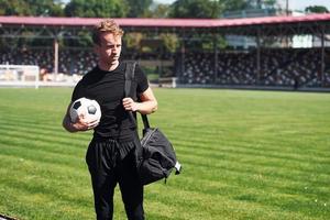 calcio giocatore su il campo. allegro giovane tipo nel nero camicia e pantaloni all'aperto a giorno foto