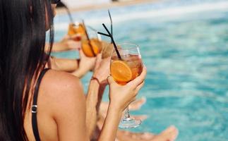 fresco cocktail nel mani. gruppo di giovane contento persone avere divertimento nel nuoto piscina a giorno foto