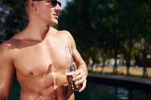 positivo giovane uomo avere un' riposo all'aperto nel nuoto piscina a giorno foto