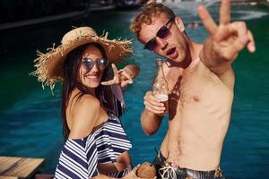 Tenere bevande nel mani. allegro coppia o amici insieme nel nuoto piscina a vacanza foto