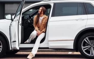 sembra al di fuori a partire dal il macchina. alla moda bellissimo giovane donna e sua moderno automobile foto